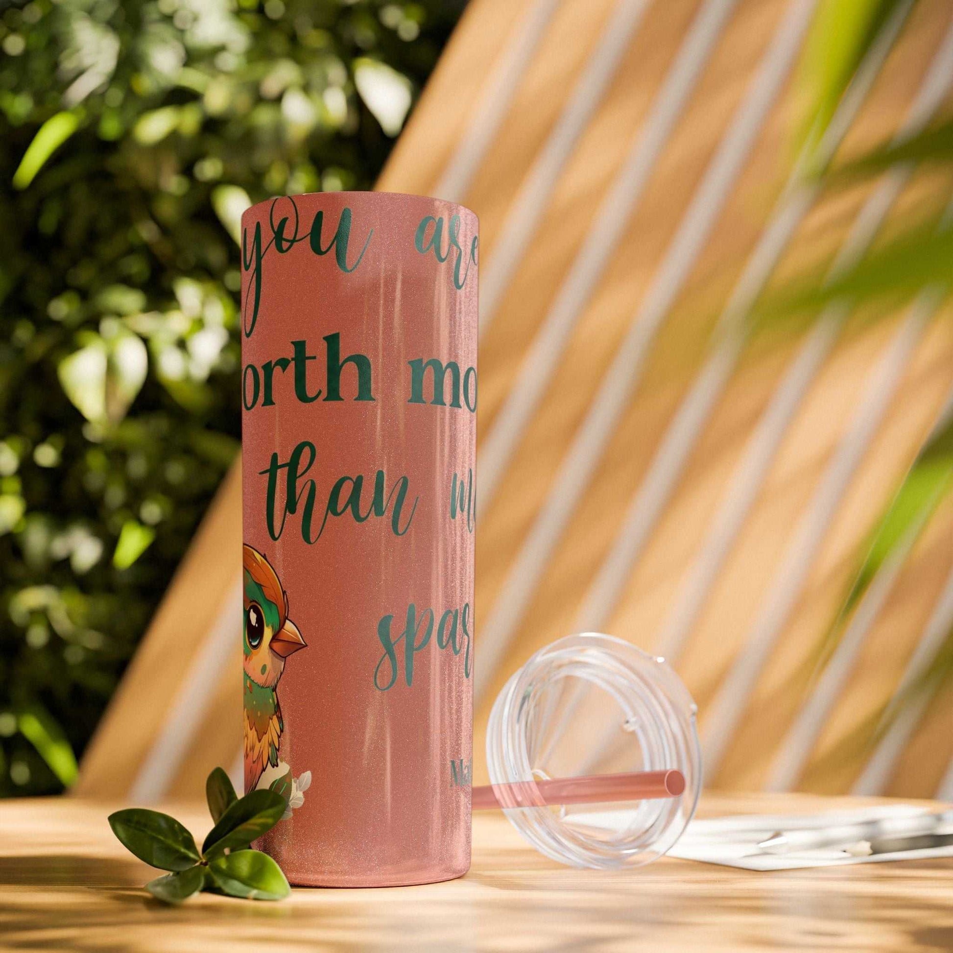 Stainless steel tumbler with motivational message "Worth More Than Sparrows," featuring a colorful bird design, plastic lid, and straw, on an outdoor table.