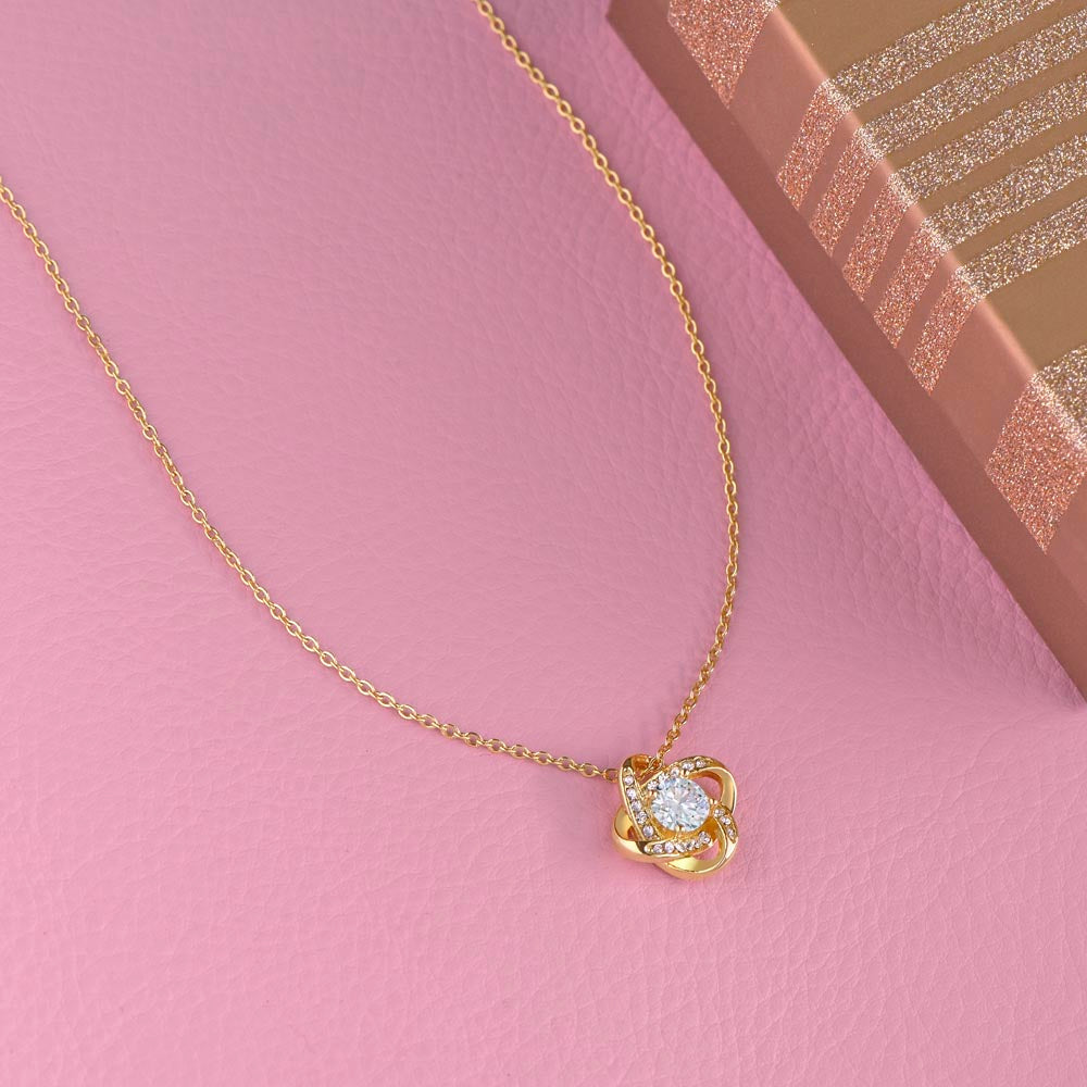 Love Knot necklace with cubic zirconia pendant on a pink background, next to a gift box.