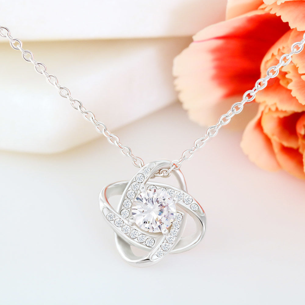 Love Knot Necklace with cubic zirconia pendant and chain, against a floral background.