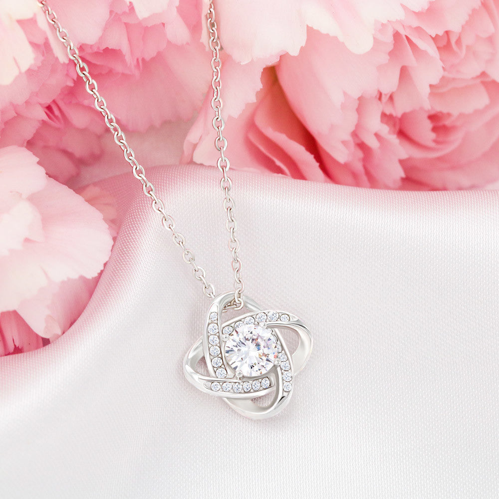 Love Knot Necklace with cubic zirconia pendant on satin, pink flower background.