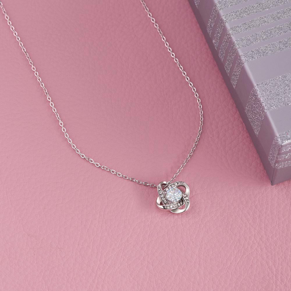 Love Knot Necklace with cubic zirconia on pink surface, gift box beside.