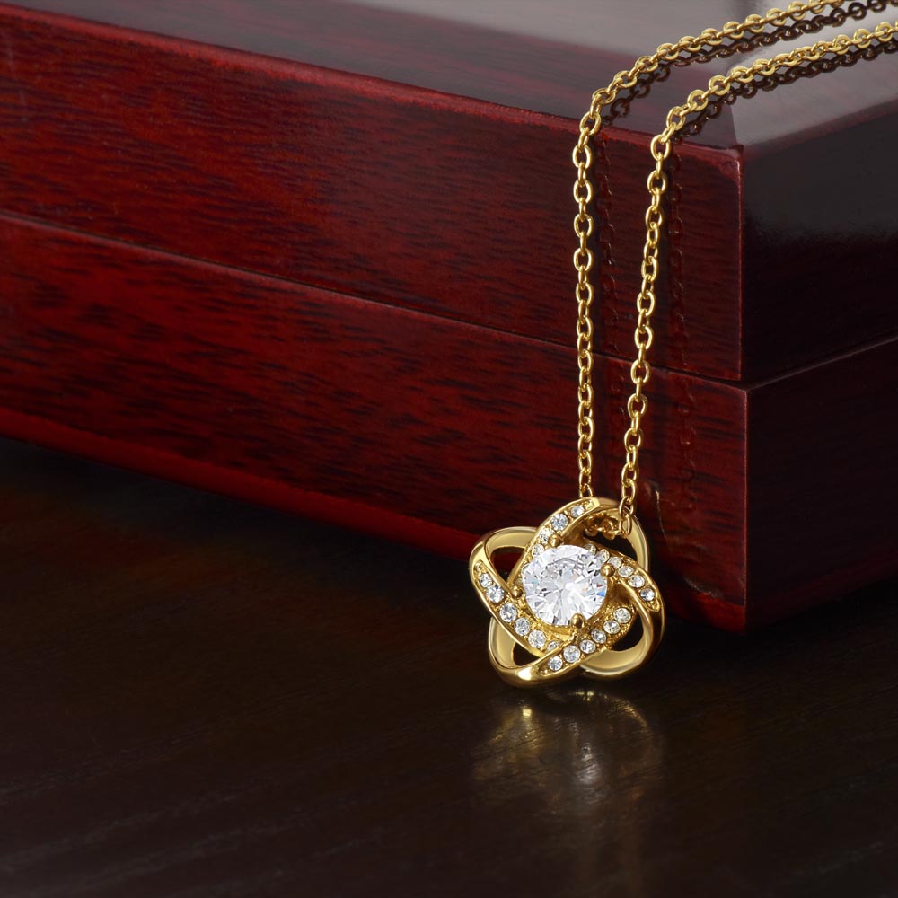 Gold love knot necklace with cubic zirconia, displayed on a wooden box.