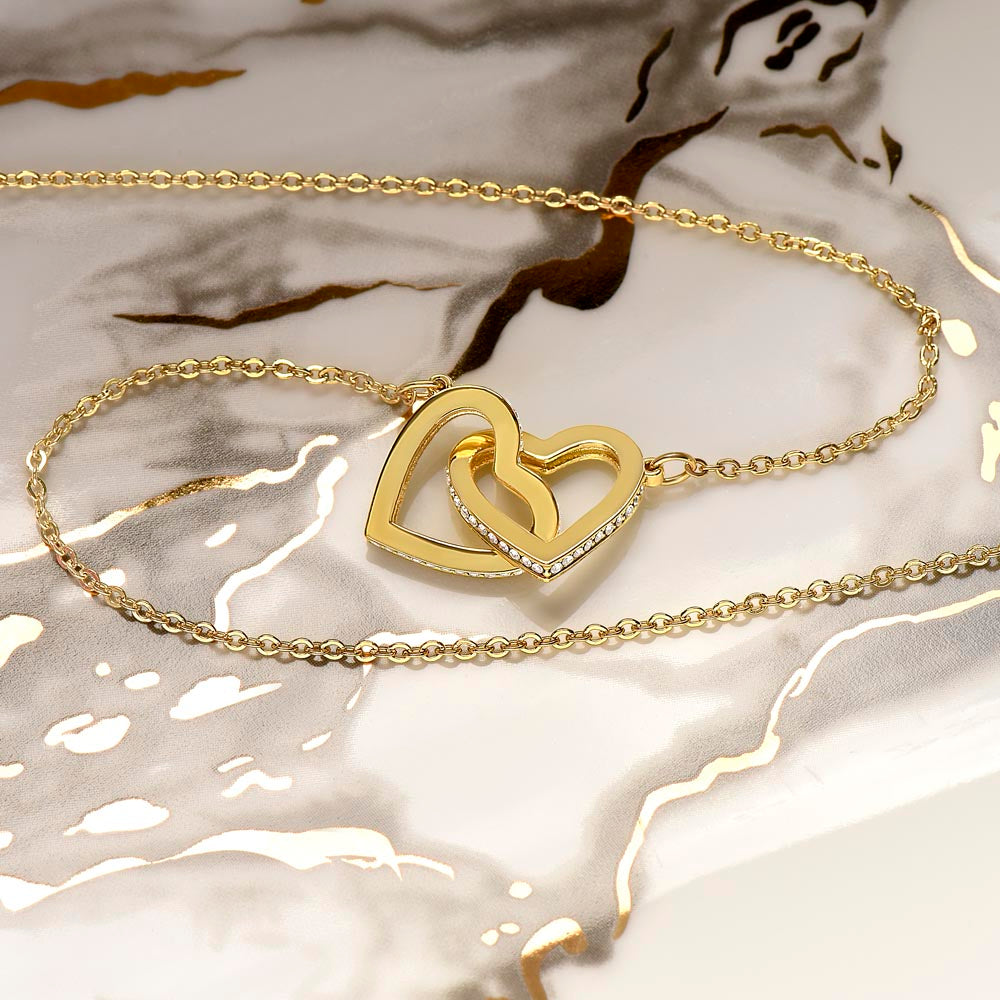 Interlocking hearts necklace with cubic zirconia in gold finish on reflective surface.