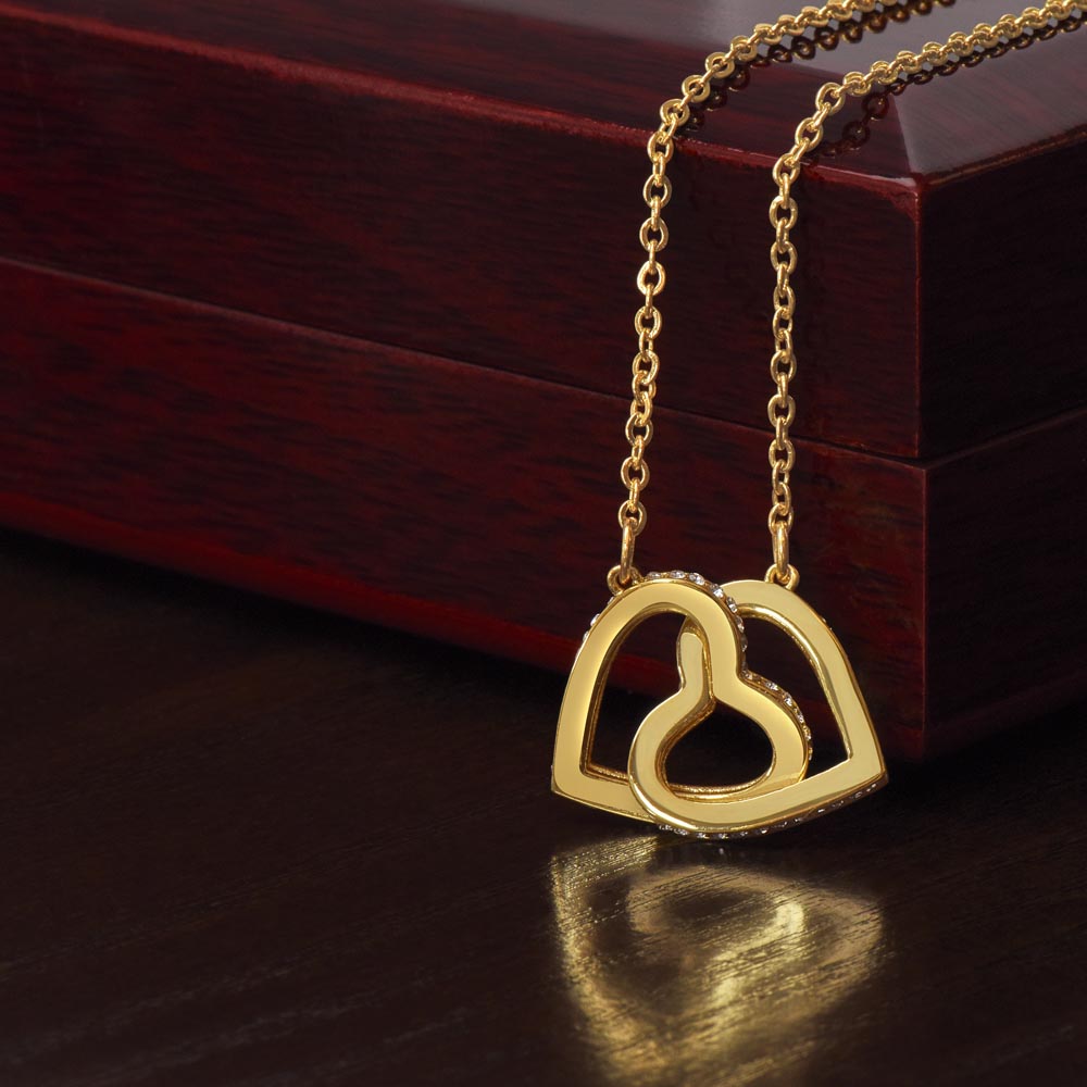 Interlocking hearts necklace with cubic zirconia on gold chain, displayed on wooden box.