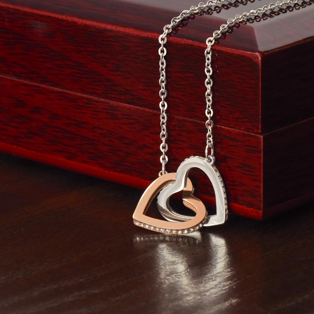 Interlocking hearts necklace with cubic zirconia crystals on a dark wood box.