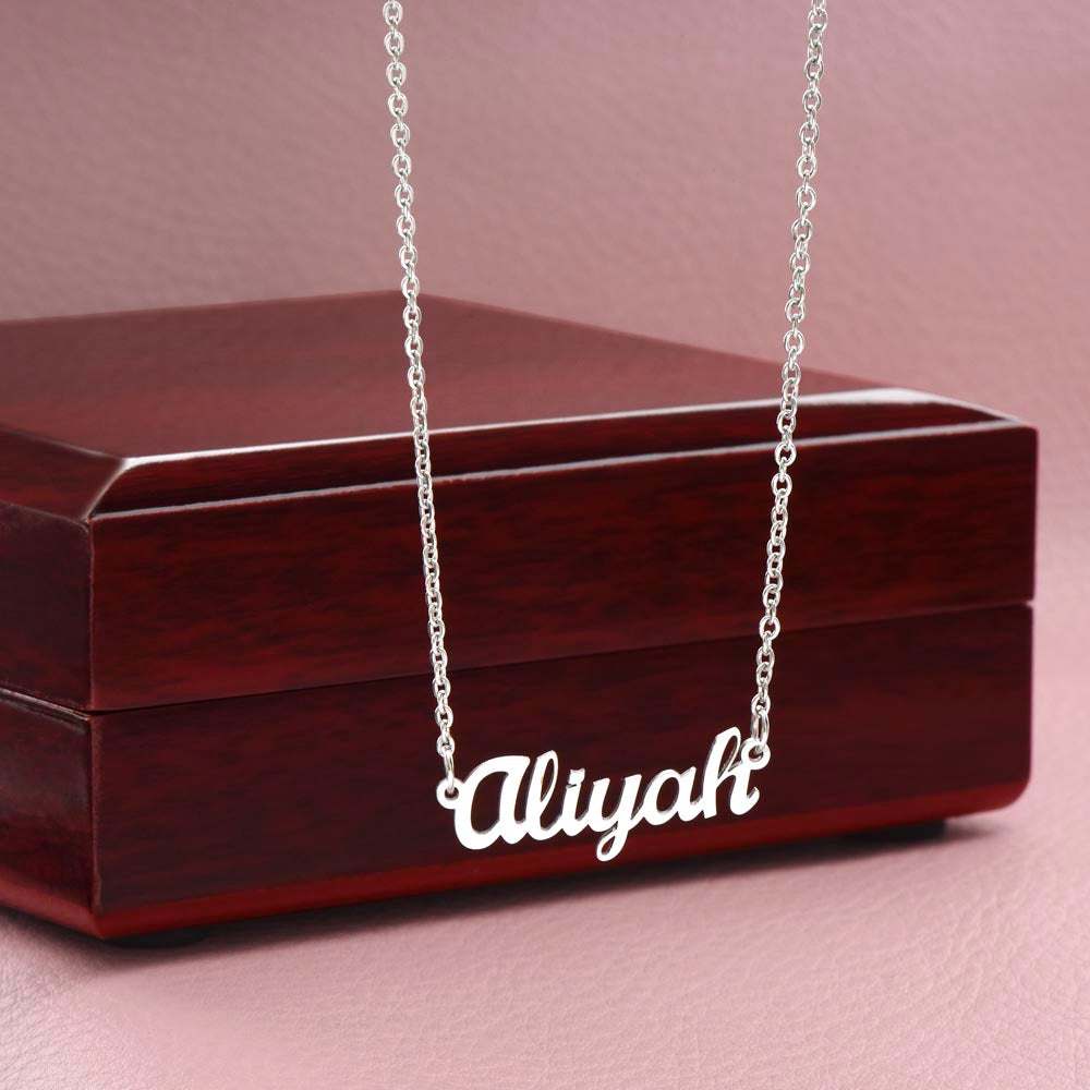 Customized name necklace in polished stainless steel on adjustable cable chain, displayed on luxury jewelry box.