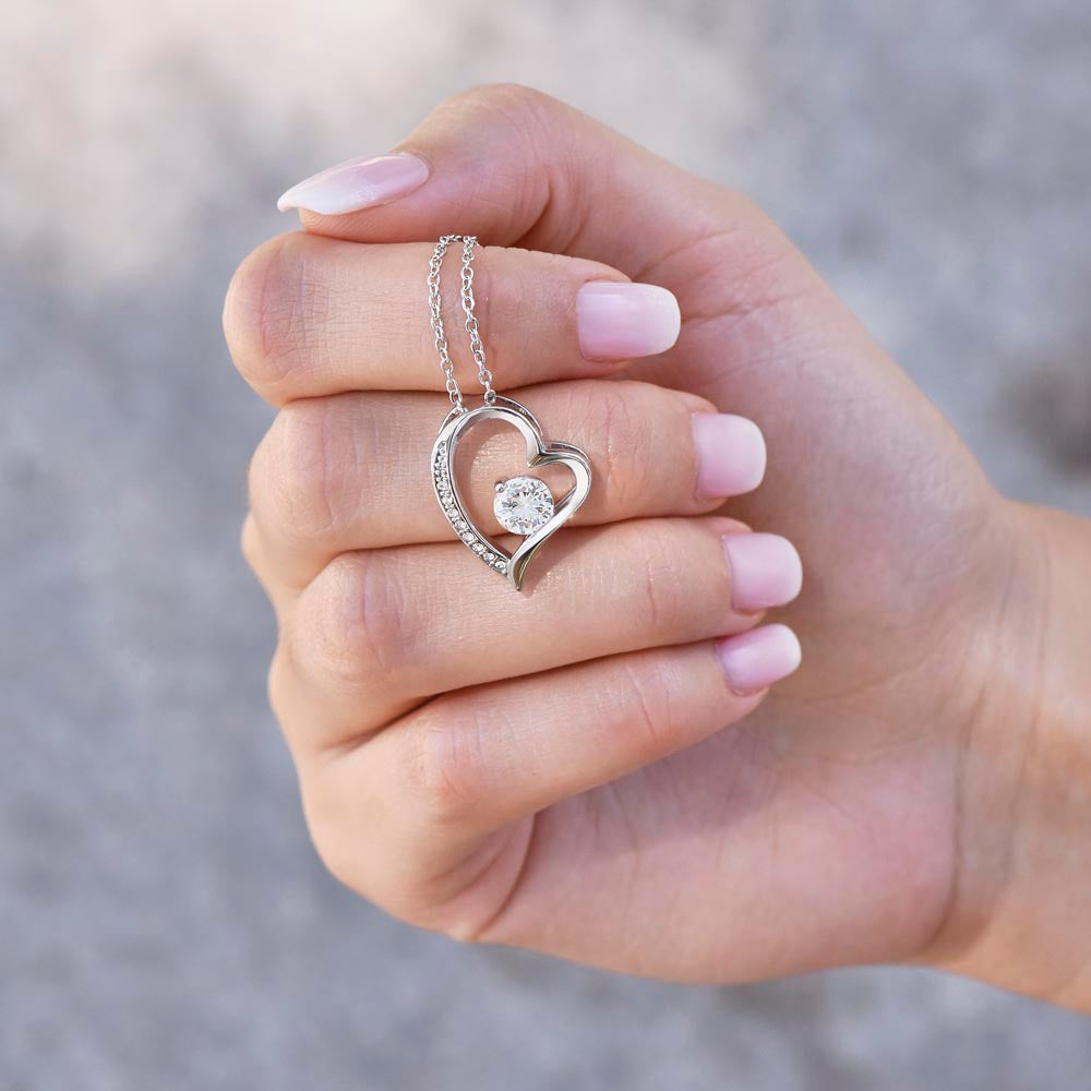 Heart-shaped necklace with cubic zirconia crystal on chain held in hand.